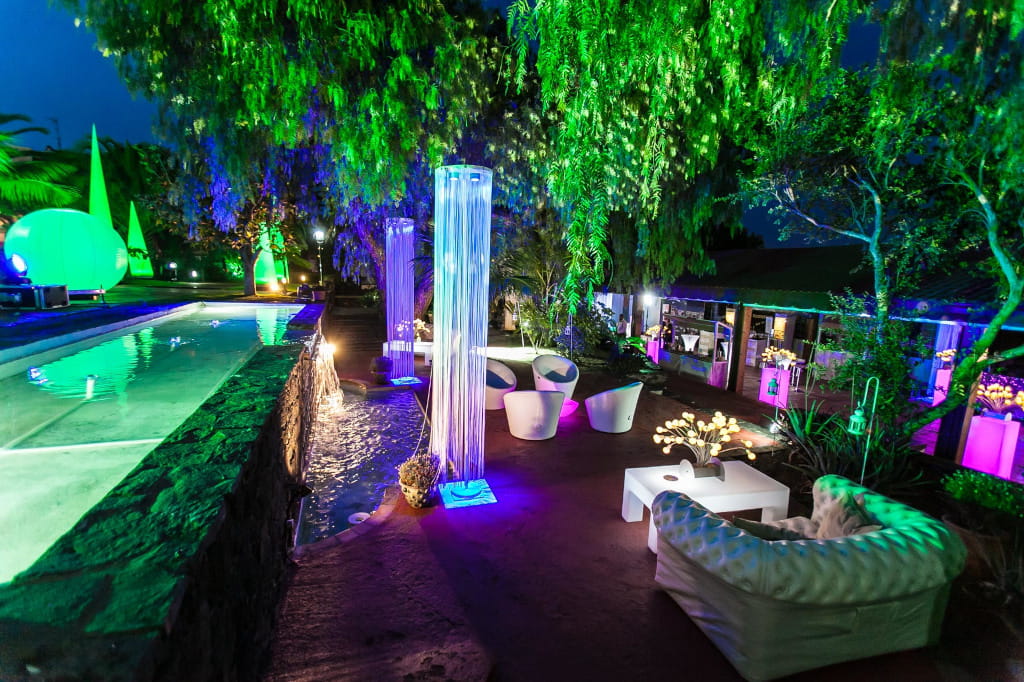 Erleuchtete Terrasse auf Teneriffa mit grünen und violetten Lichtern auf Möbeln und Vegetation.