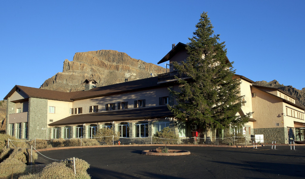 Gebäude mit bergigem Hintergrund und großem Baum in El Teide, Teneriffa.
