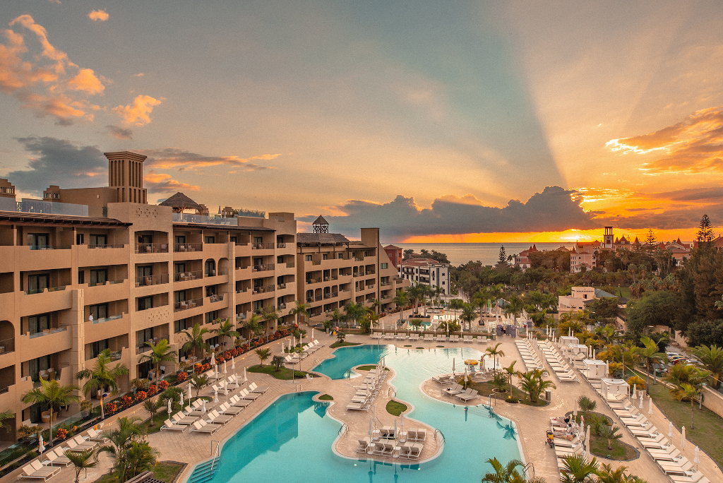Hotelkomplex mit Schwimmbad bei Sonnenuntergang auf Teneriffa, orangefarbener Himmel im Hintergrund.