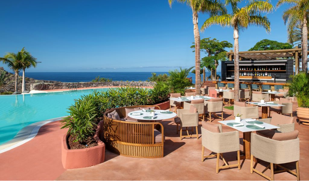 Terrasse mit Tischen und Stühlen am Pool und Meerblick auf Teneriffa.