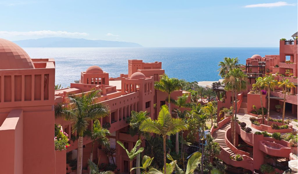 Terrakottafarbene Gebäude mit Meeresblick auf Teneriffa, umgeben von Palmen.