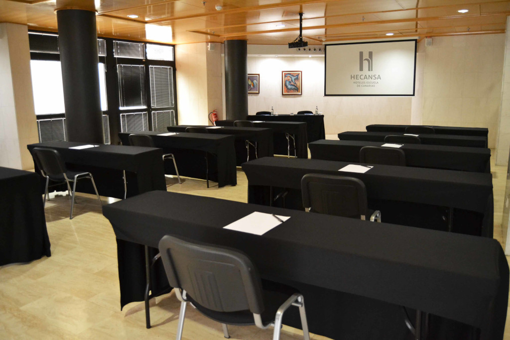 Konferenzraum mit schwarzen Tischen, Stühlen und Projektionsleinwand in Hecansa, Teneriffa.