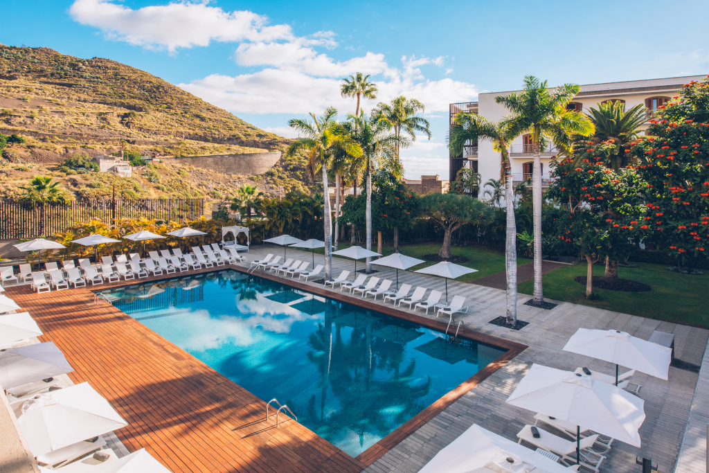 Ein Schwimmbecken, umgeben von Liegeplätzen und Sonnenschirmen, mit Bergen im Hintergrund auf Teneriffa.