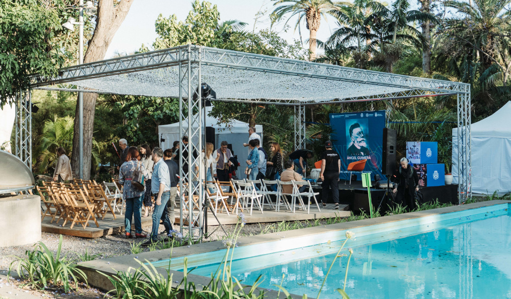 Veranstaltung in einem Garten auf Teneriffa mit Sitzgelegenheiten und einem Schild von Ángel Guimerá in der Nähe eines Schwimmbeckens.