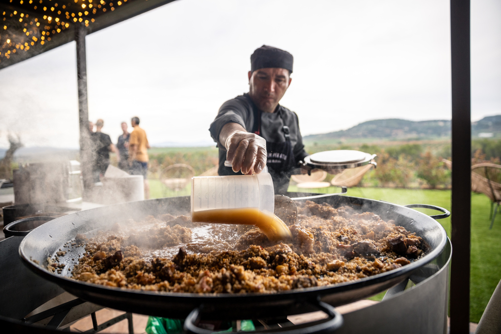 Koch gießt Brühe in eine große Paella im Freien auf Teneriffa.