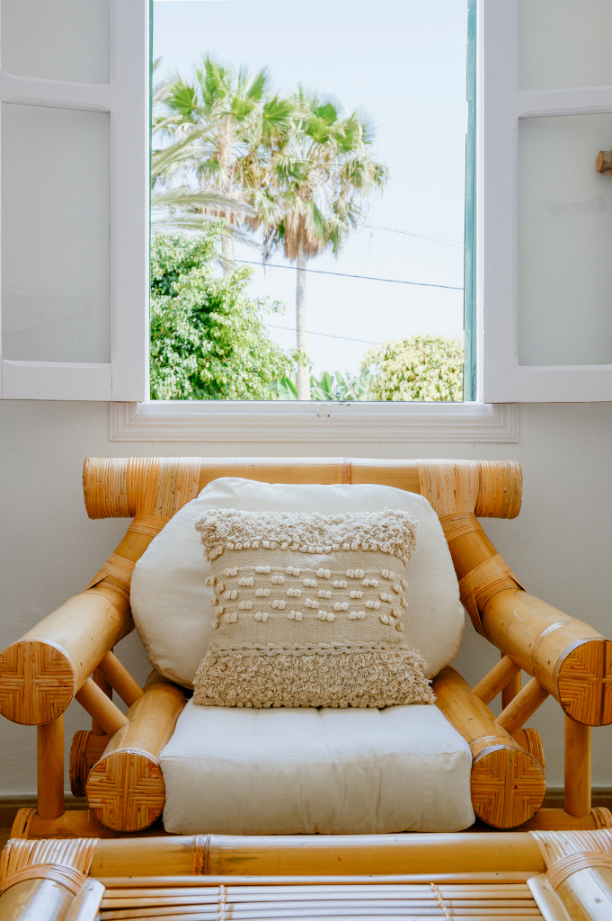 Rattan-Sessel mit Kissen vor offenem Fenster und Palmenblick in Tenerife.