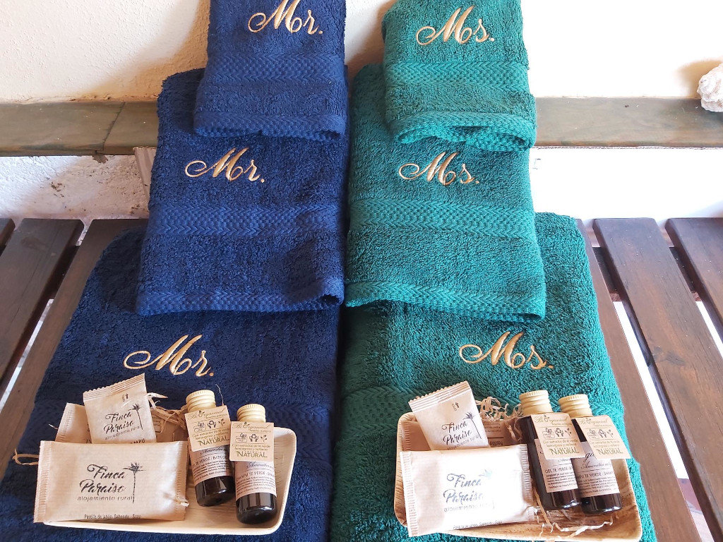 Handtücher mit Mr. und Ms. bestickt, daneben Finca Paraíso Toilettenartikel.