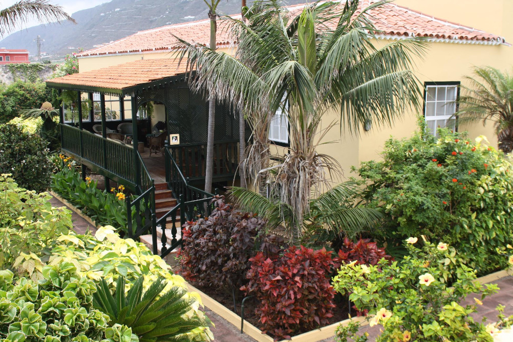 Gelbes Haus mit Veranda und tropischen Pflanzen in einem Garten in Tenerife.