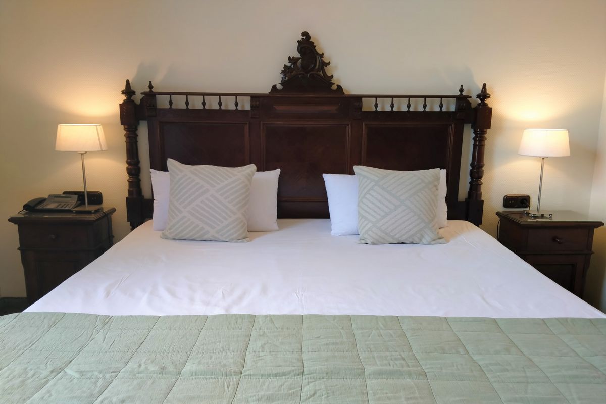 Großes Bett mit Holzkopfteil, Kissen und Lampen in Hotelzimmer in Tenerife.