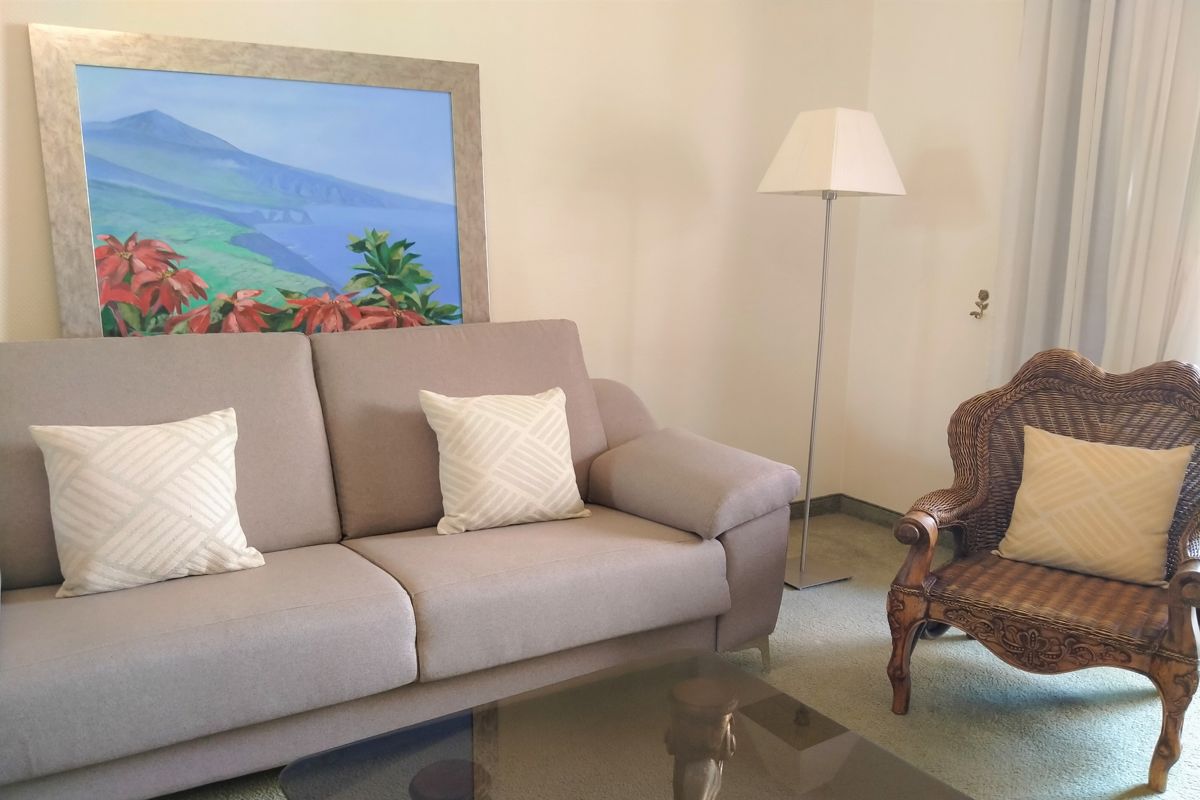 Graues Sofa mit zwei Kissen, gemaltes Bild von Landschaft, Lampe und Sessel.