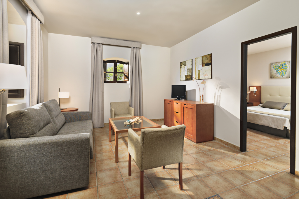 Wohnzimmer mit Sofa, Tisch, Sessel und Zugang zu Schlafzimmer in Hotel in Tenerife.