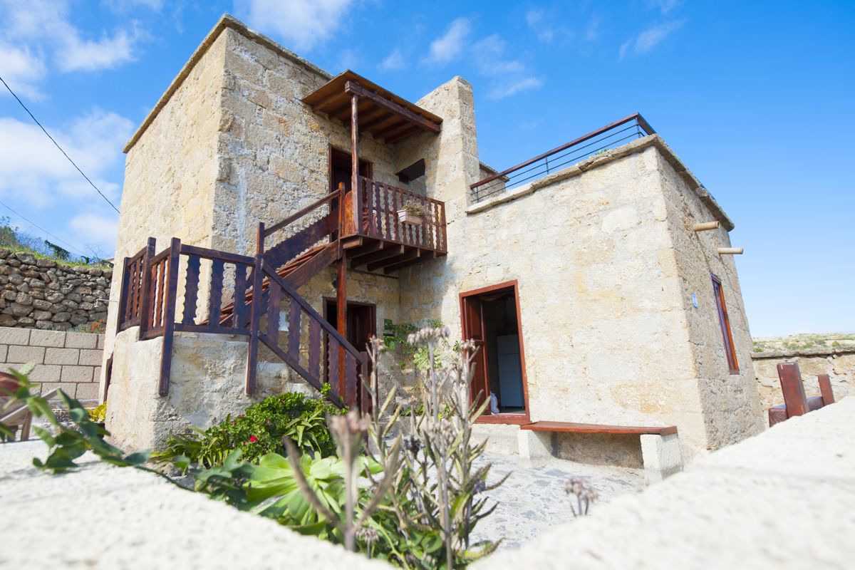 Steinhaus mit Holztreppe in Teneriffa, umgeben von Blumen und blauem Himmel.