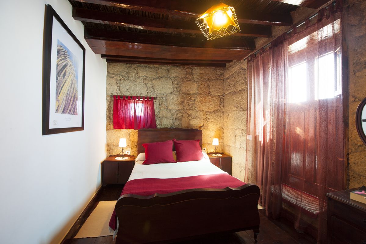 Schlafzimmer mit Doppelbett, roten Kissen, Steinwand und Lampen in El Sauzal, Teneriffa.