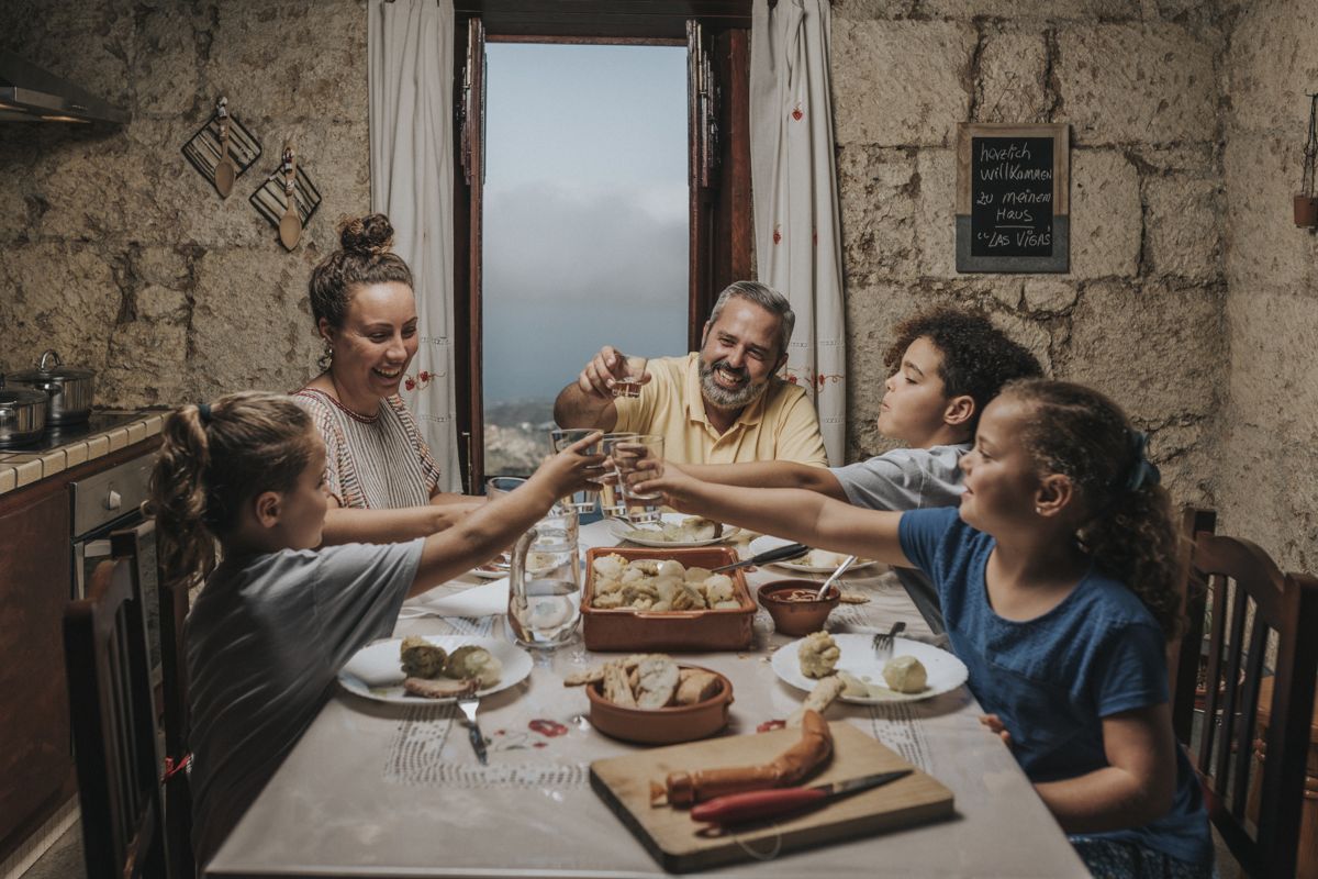 Familie stoßt beim Abendessen in einem rustikalen Haus in La Laguna an.