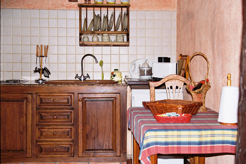 Kleine Küche in Teneriffa mit Holzmöbeln, Geschirrregal und Tisch mit gestreifter Tischdecke.