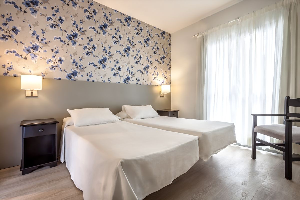 Zwei Einzelbetten im Hotelzimmer in Tenerife mit blumigem Hintergrund.