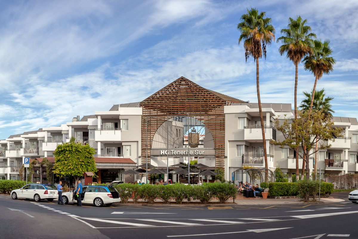 HG Tenerife Sur mit Palmen und geparkten Autos an der Straße.