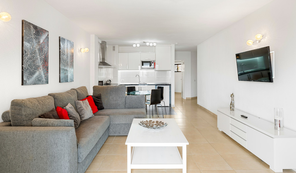 Wohnzimmer mit grauem Sofa, Fernseher an der Wand und Blick auf die Küche in Tenerife.