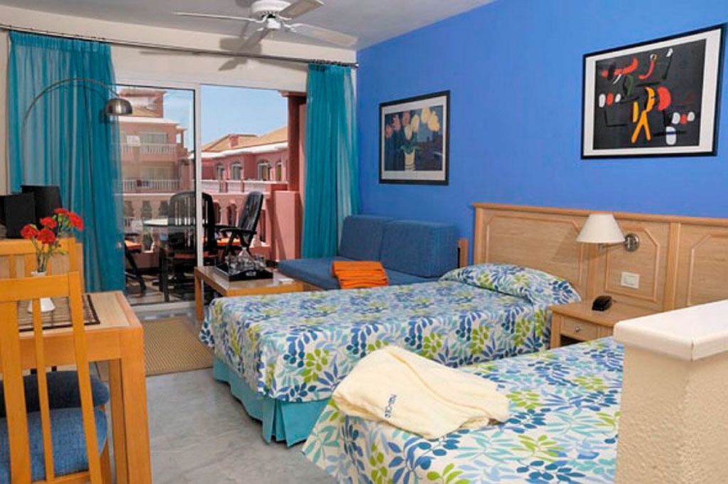 Zweibettzimmer mit blauen Vorhängen und Balkonblick in Teneriffa.