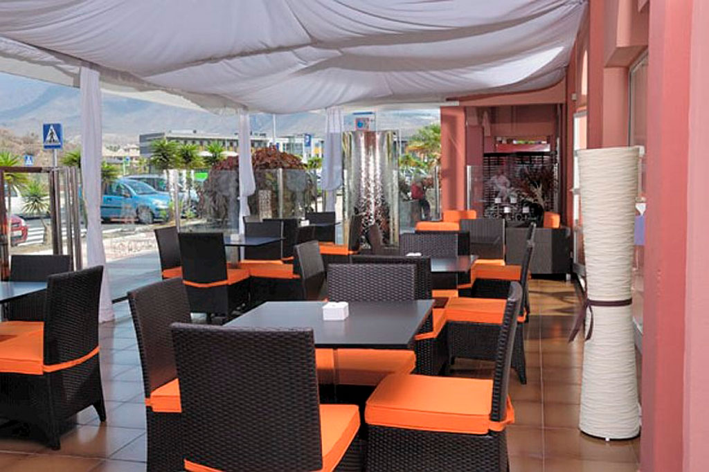 Restaurant-Terrasse mit schwarzen Stühlen und orangen Kissen in Teneriffa.