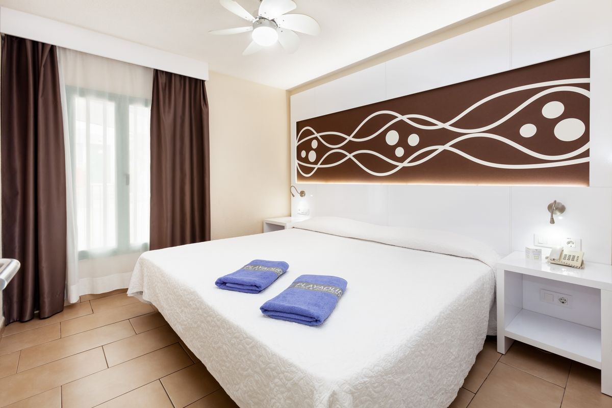 Hotelzimmer mit Doppelbett, zwei blauen Handtüchern mit Aufschrift PLAYAOLID, in Adeje, Teneriffa.