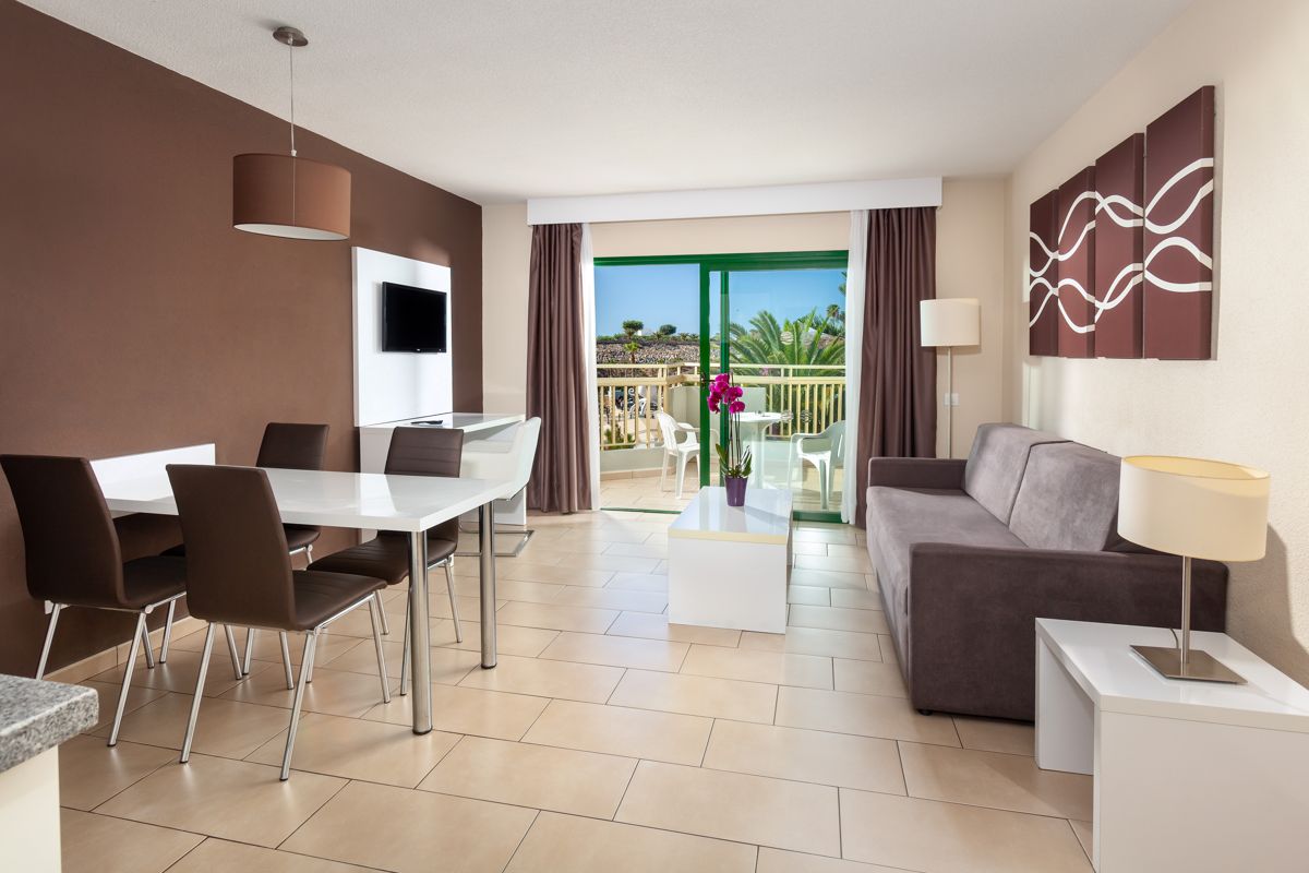 Wohnzimmer mit Sofa, Esstisch und Balkonblick auf Palmen in Teneriffa.