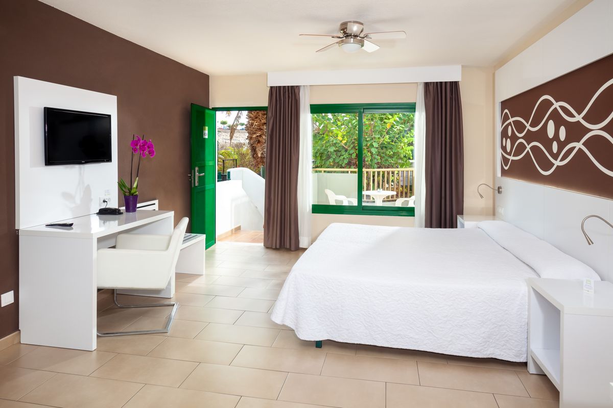 Helles Hotelzimmer in Teneriffa mit Bett, Schreibtisch, TV und Balkon.