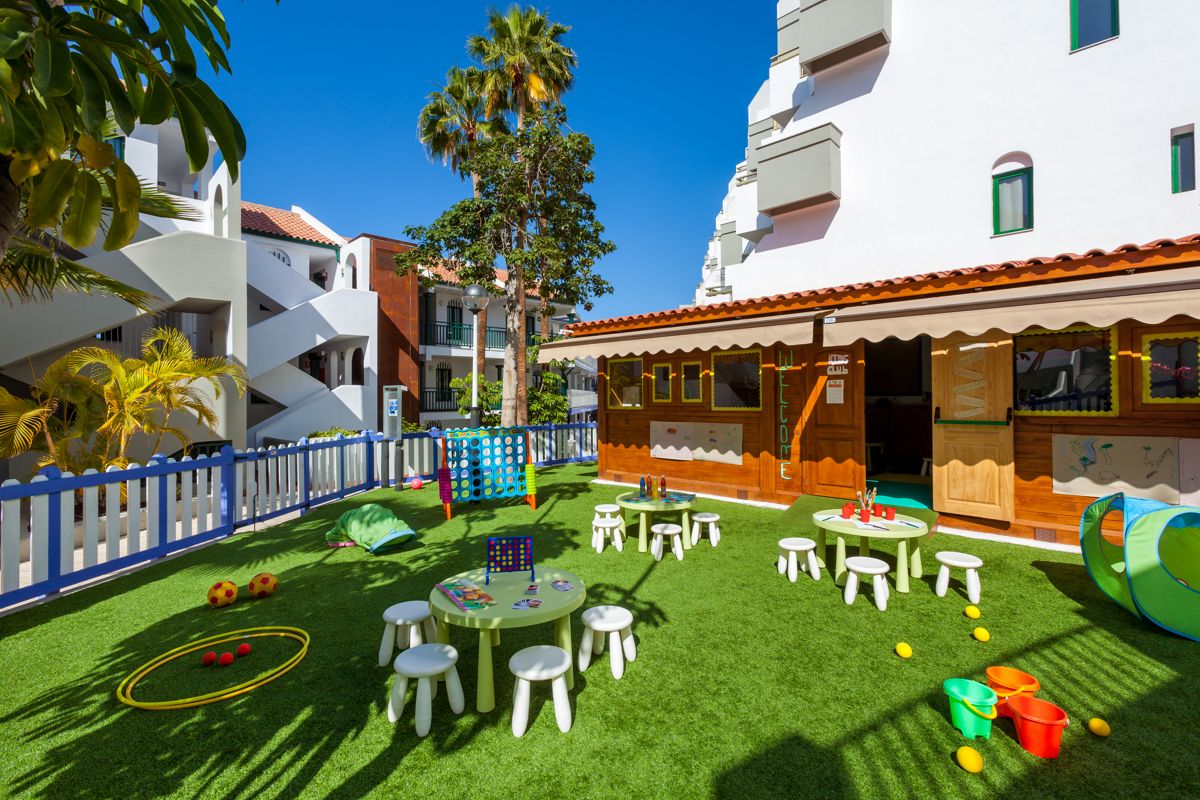 Spielplatz in Costa Adeje mit grüner Wiese, Kindertischen und Spielzeug.