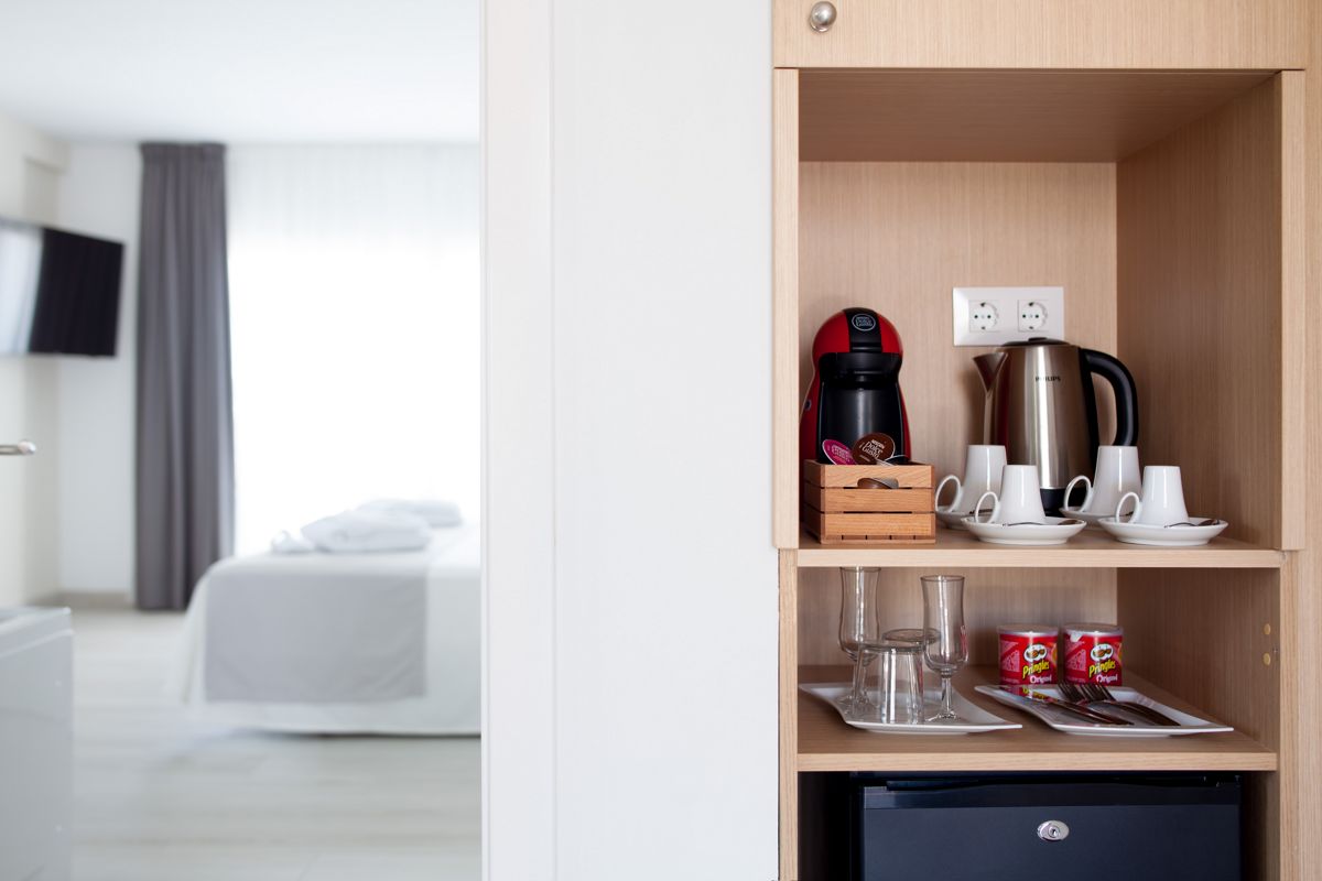 Miniküche mit Kaffeemaschine, Wasserkocher und Geschirr in einem Hotelzimmer in Teneriffa.