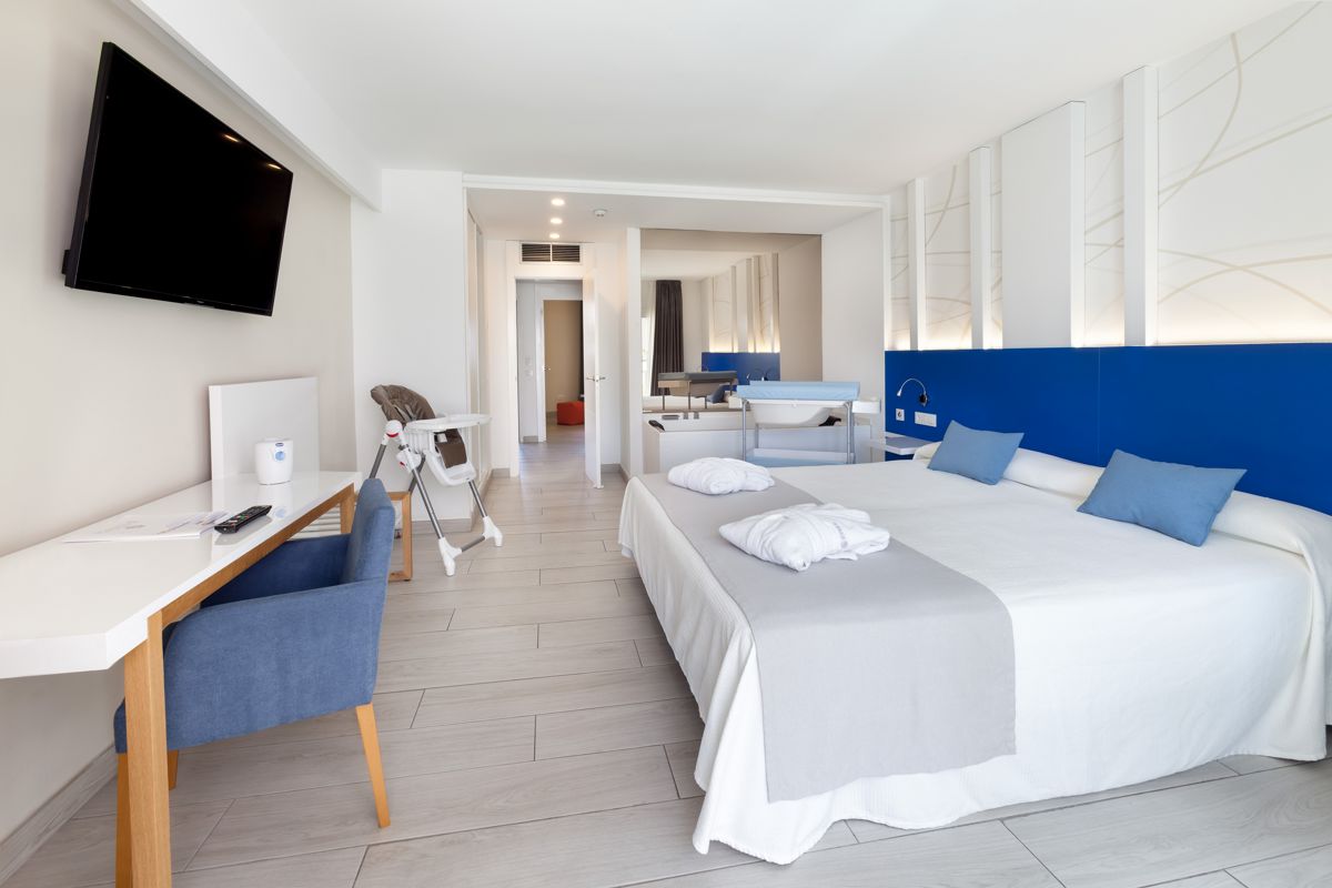 Modernes Hotelzimmer in Tenerife mit Doppelbett, TV, Schreibtisch und Hochstuhl.