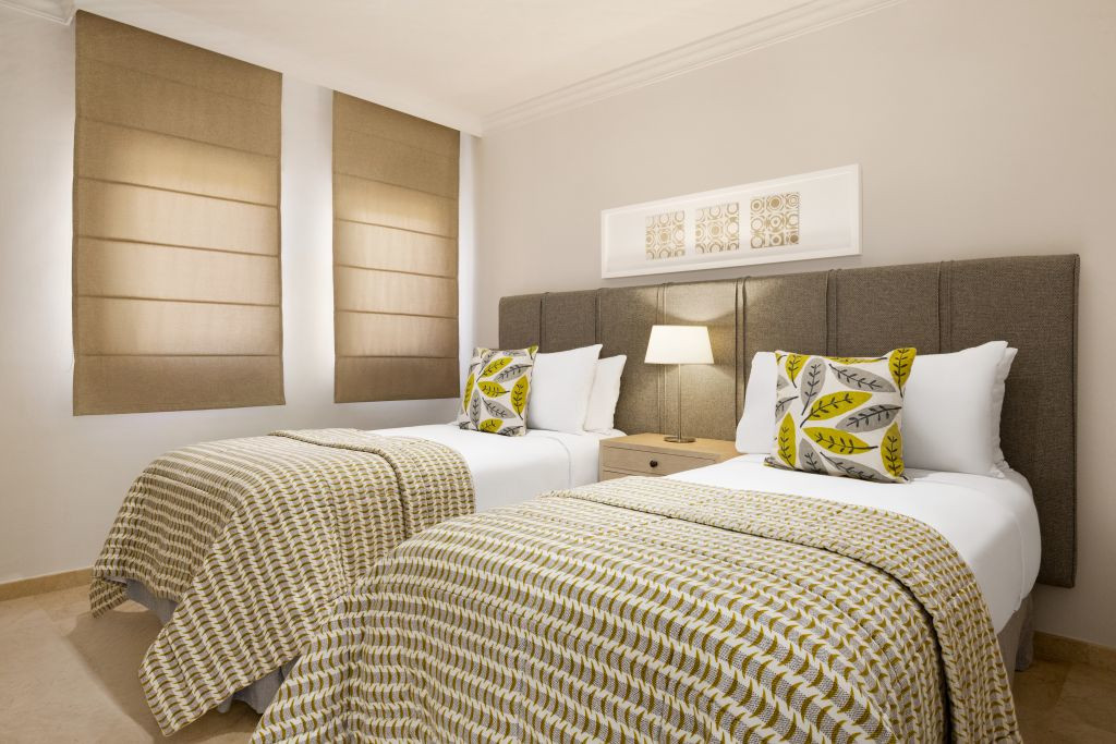 Zwei Einzelbetten im Hotelzimmer in Teneriffa mit Lampe und Kunstwerk an der Wand.