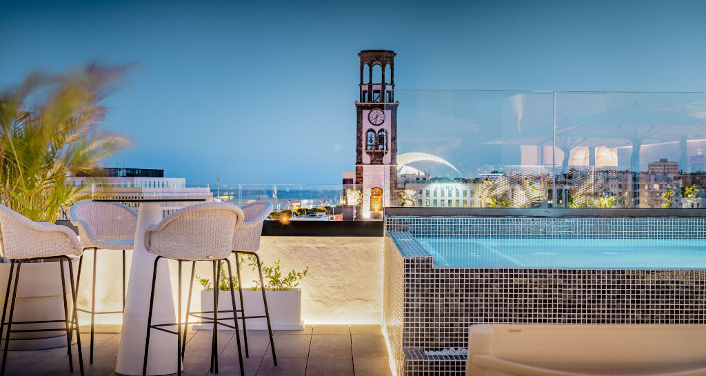 Dachterrasse mit Pool und Blick auf Uhrturm von Santa Cruz de Tenerife bei Abenddämmerung.