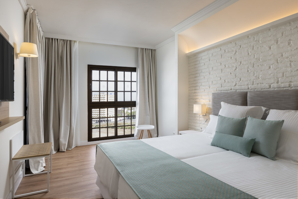 Hotelzimmer in Teneriffa mit Doppelbett, Kissen und Fenster mit Blick.