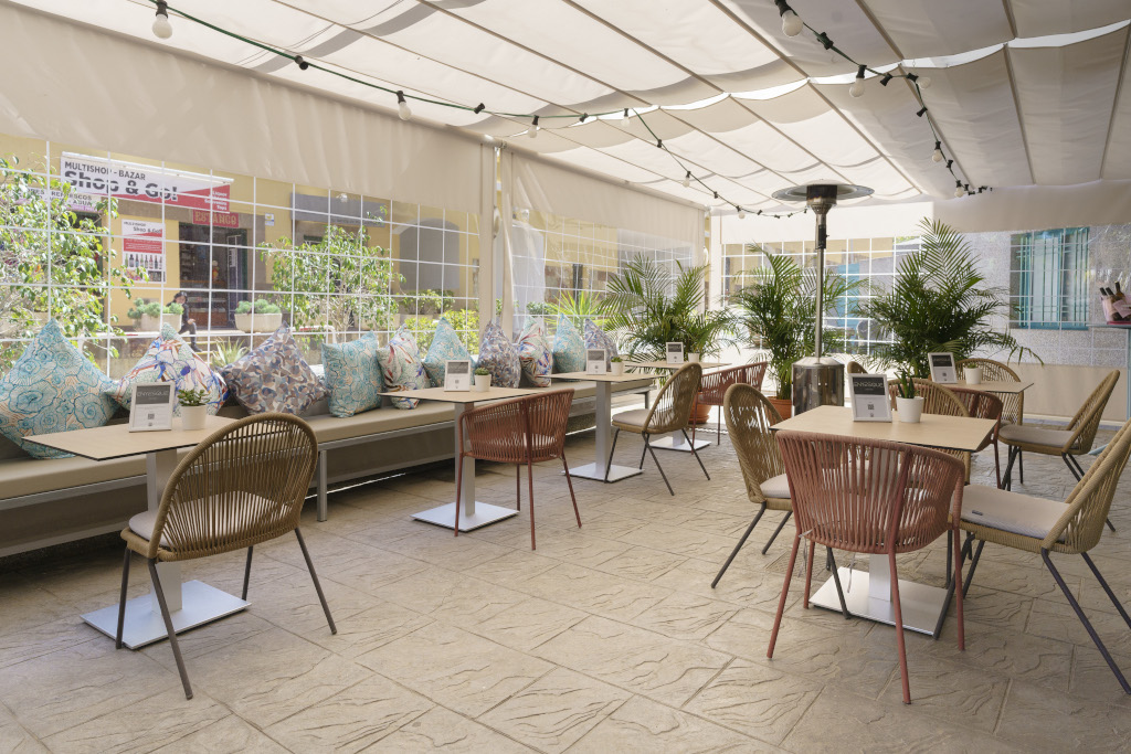 Überdachte Terrasse in einem Café in Tenerife mit Tischen, Stühlen und Pflanzen.