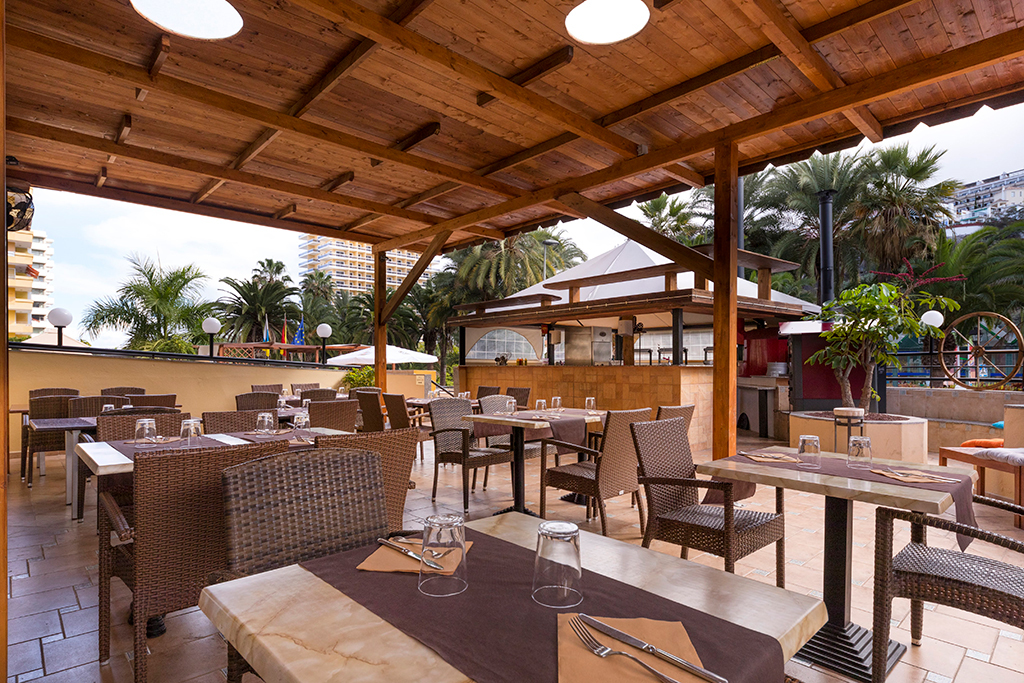 Offene Terrasse mit Tischen und Stühlen. Palmen im Hintergrund in Puerto de la Cruz.