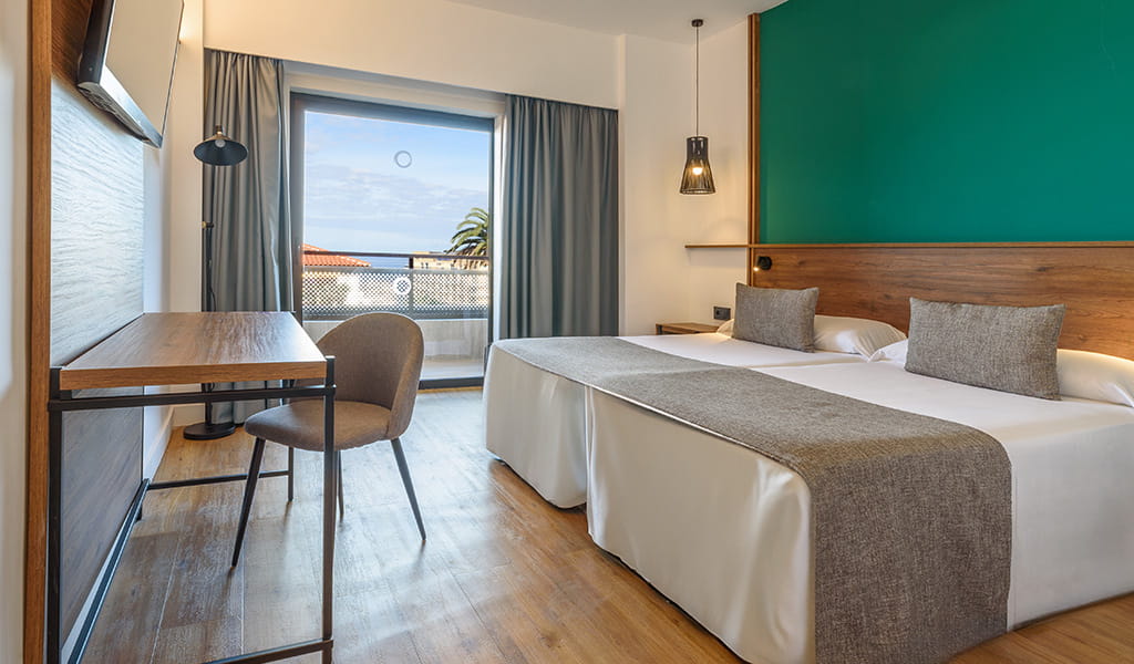 Hotelzimmer in Puerto de la Cruz mit zwei Betten, Schreibtisch und Balkon mit Meerblick.