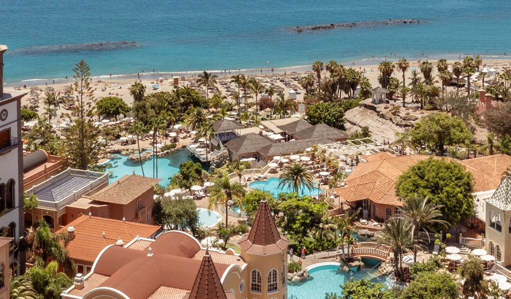 Strand und Hotelanlage in Costa Adeje, Teneriffa, mit Palmen und Pools.