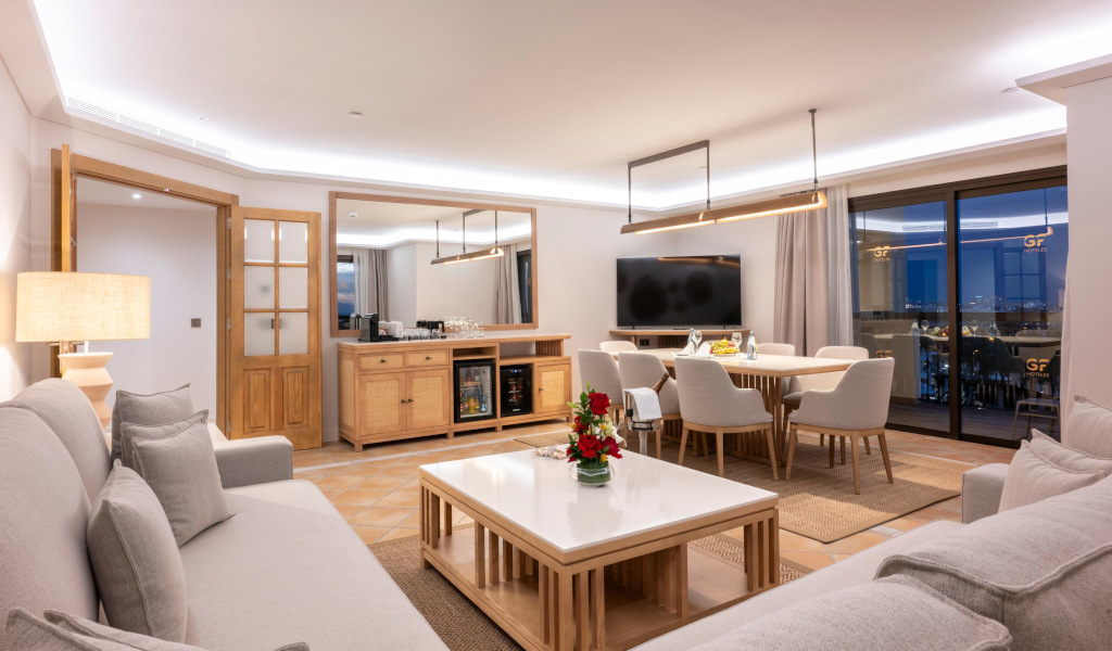 Wohnzimmer eines Hotels in Teneriffa mit Sofa, Esstisch und Balkonblick.