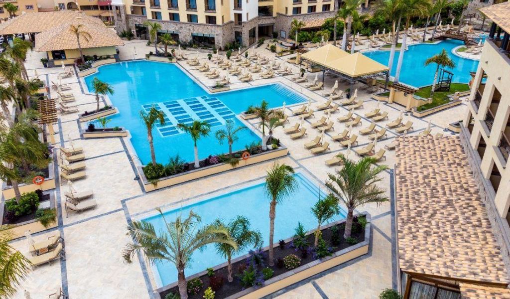 Außenpoolbereich eines Resorts in Adeje, Teneriffa, mit Liegestühlen und Palmen.