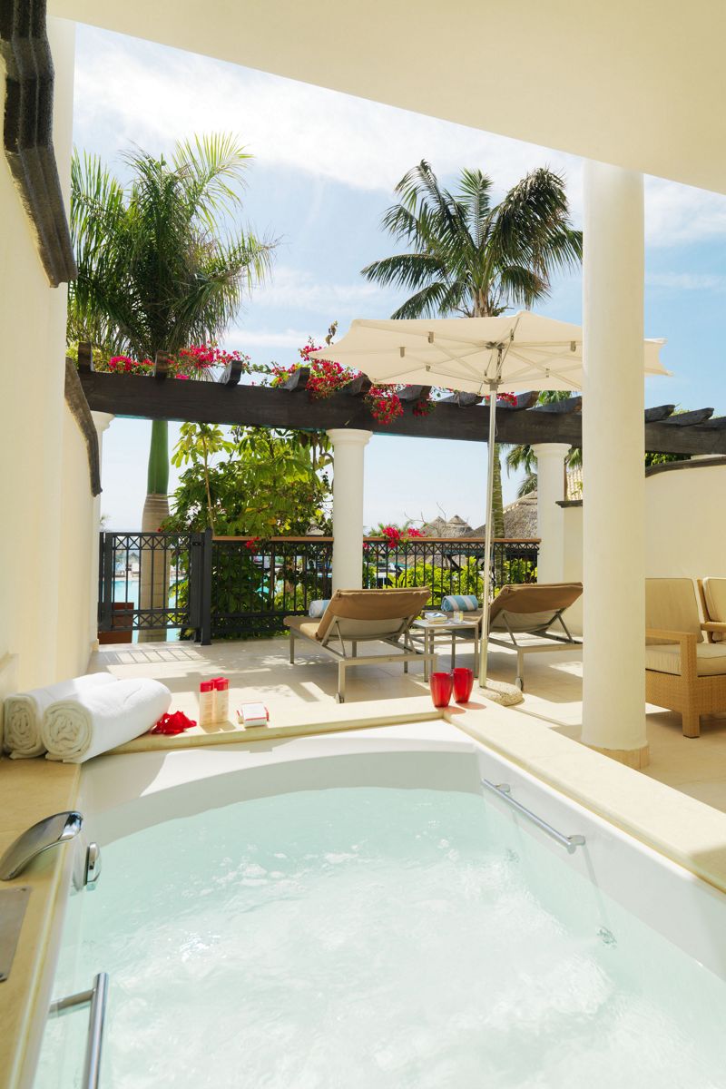 Terrasse mit Liegestühlen, Sonnenschirm und Whirlpool, umgeben von Palmen in Tenerife.