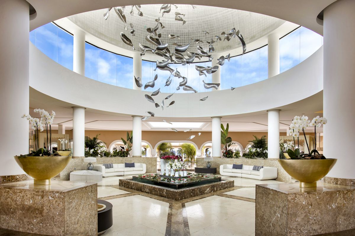 Offener, heller Hotellobby-Bereich in Teneriffa mit Pflanzen und moderner Kunstinstallation.