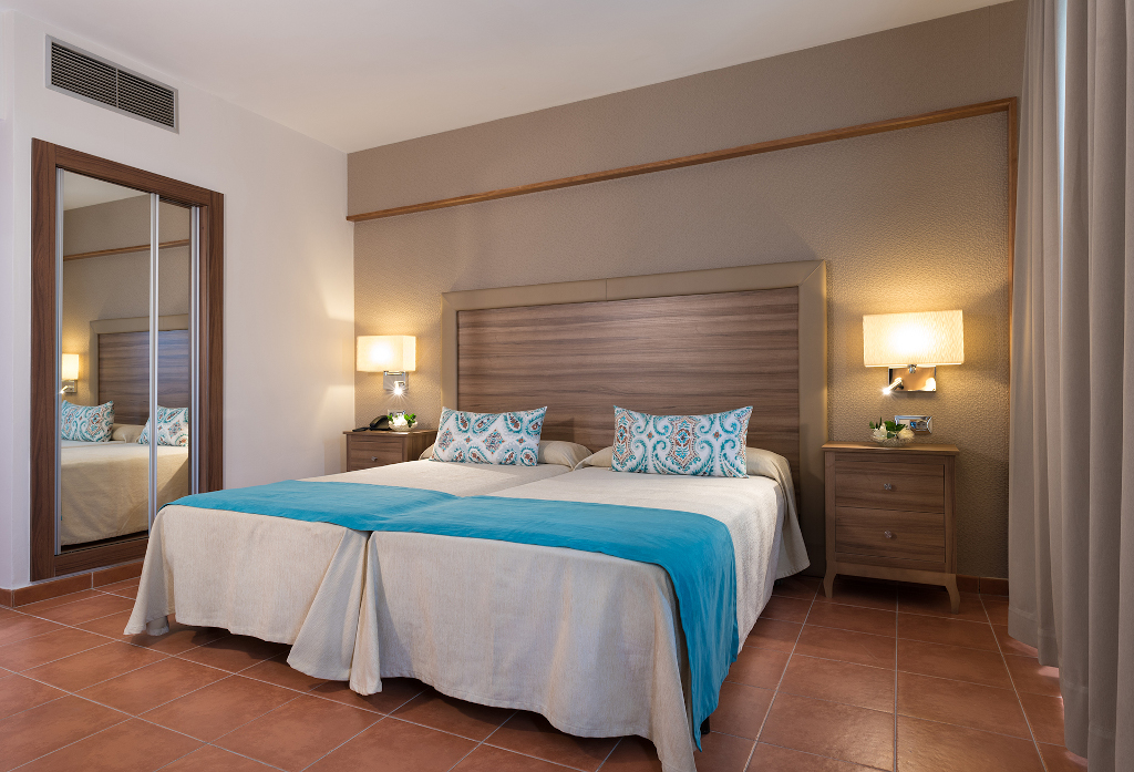 Zwei Betten mit blauen Decken und Spiegel in Hotelzimmer in Adeje, Teneriffa.