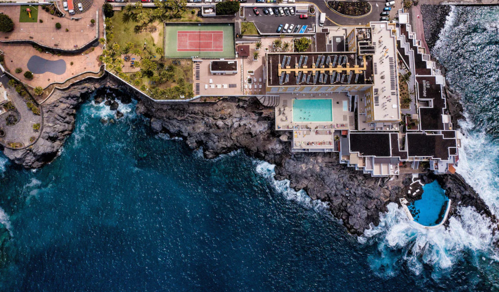 Gebäude mit Pool und Tennisplatz an der Küste von Tenerife, umgeben vom Meer.
