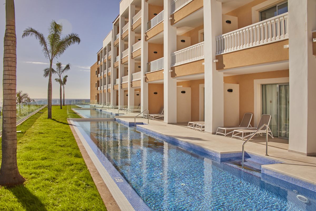 Mehrstöckiges Hotel in Teneriffa mit Pool und Palmen im Sonnenschein.