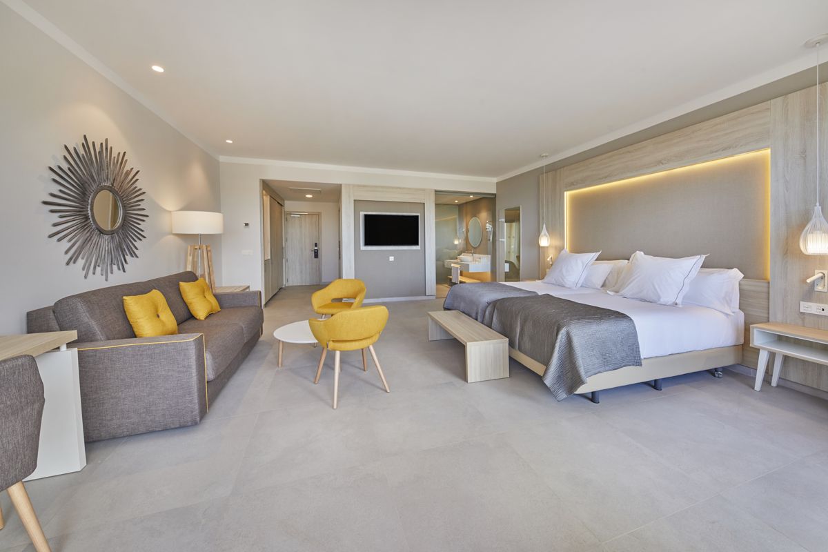 Moderne Hotelsuite in Teneriffa mit Doppelbett, Sofa und gelben Stühlen.