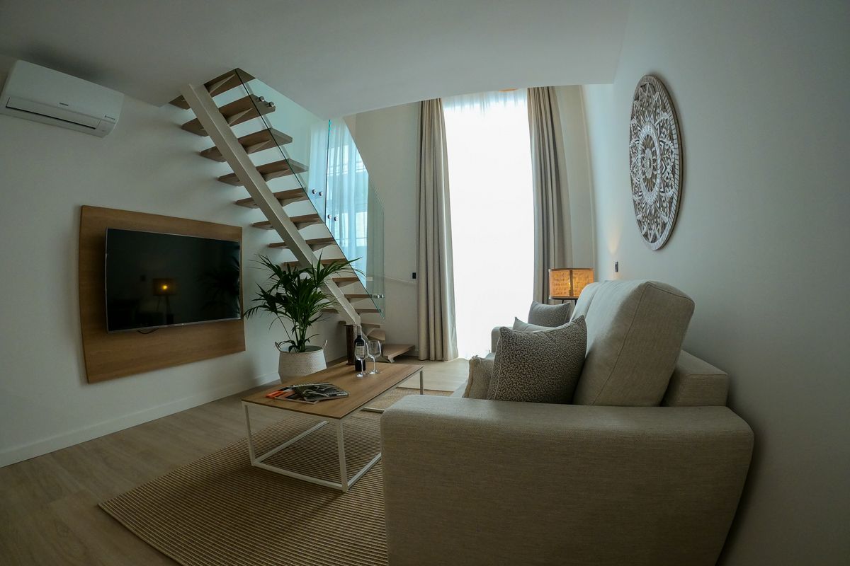 Wohnzimmer in Teneriffa mit Sofa, Tisch, Pflanzen und offenem Treppenaufgang.