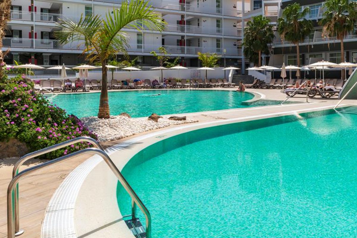 Poolbereich im Hotel von Los Cristianos, Teneriffa, mit Liegestühlen und Palmen.