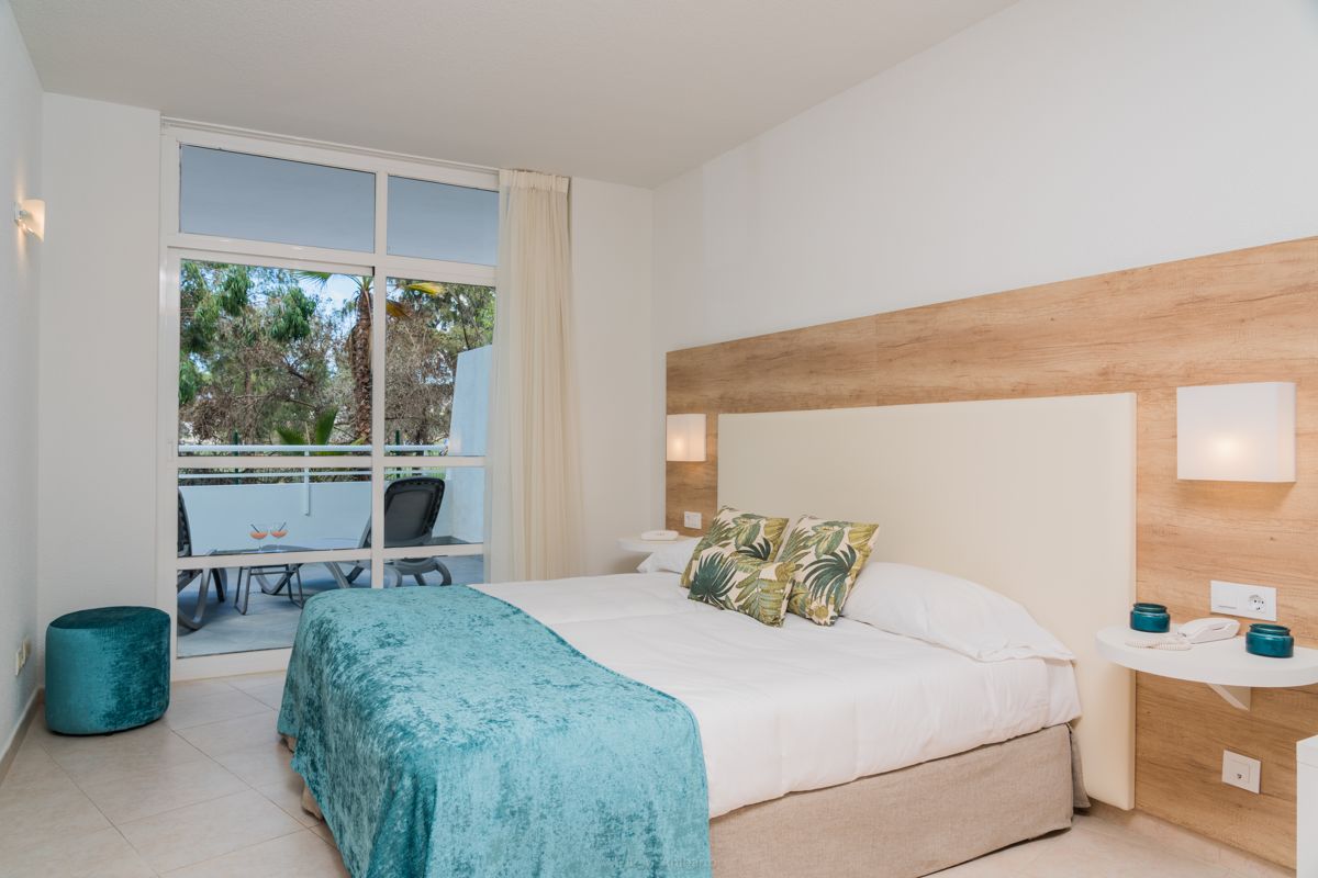 Schlafzimmer mit Doppelbett, Kissen mit Palmendruck, Terrasse mit Stühlen in Teneriffa.