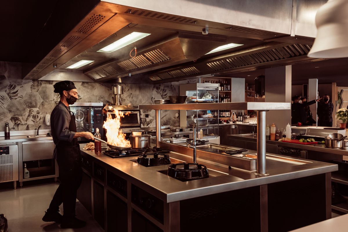 Koch bereitet Gericht mit Flammen in Restaurantküche in Santa Cruz de Tenerife zu.