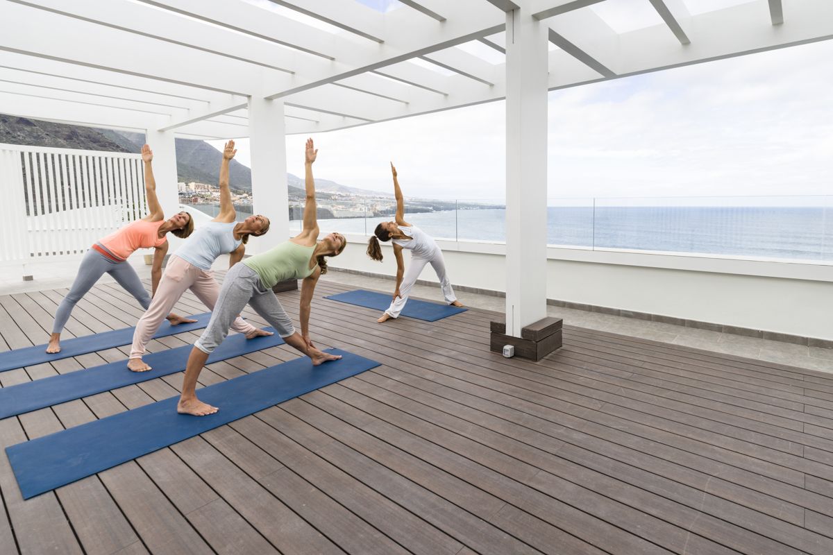 Personen praktizieren Yoga auf einer Terrasse mit Meerblick in Tenerife.